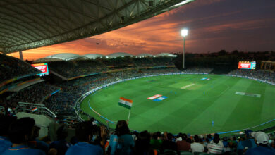 A packed cricket stadium at sunset with fans watching an India-Pakistan match, an Indian flag waving in the foreground.